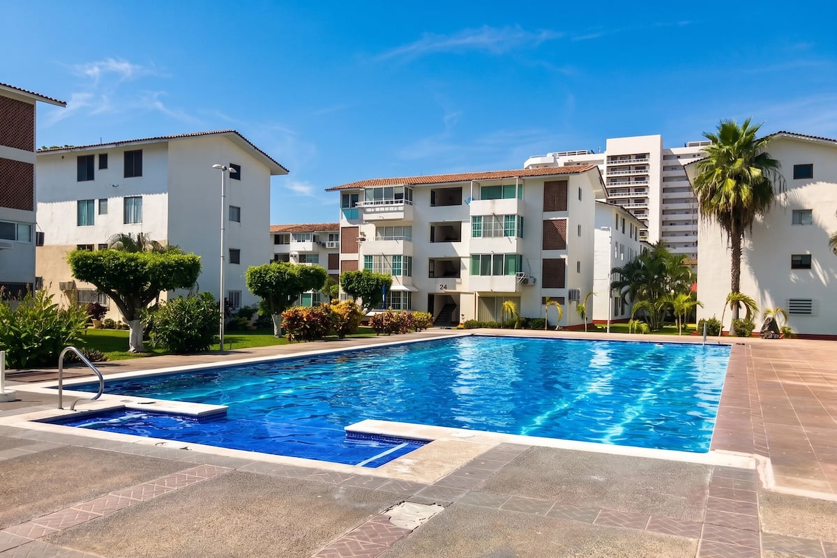 A swimming pool with a clear blue water, surrounded by a tiled deck.