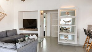 A modern living room with a grey sofa, a flat-screen TV, a glass coffee table, and a built-in shelving unit with decorative items. - La Marina Condominios by Monyxbnb (Puerto Vallarta)