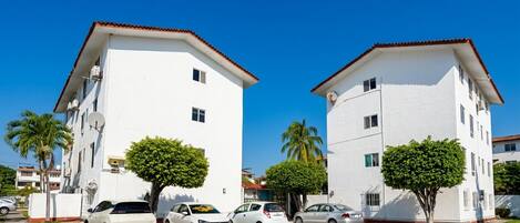 A white building with a red roof, surrounded by parked cars and palm trees.