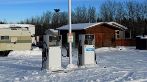 Une station-service avec deux pompes à essence, une cabane en bois et un camping-car, le tout dans un paysage enneigé.