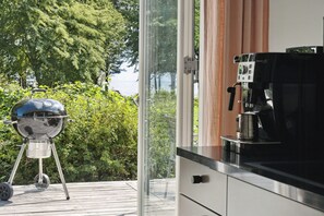 Eine moderne Küche mit integriertem Kaffeeautomaten, einer Glastür, die auf eine Terrasse führt, und einem Grill im Freien.