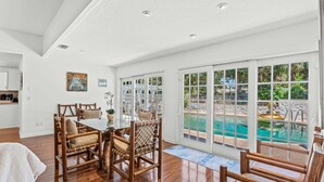 Ein geräumiges Zimmer mit Essbereich, großen Fenstern und Blick auf einen Swimmingpool.