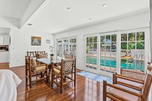 Ein geräumiges Zimmer mit Essbereich, großen Fenstern und Blick auf einen Swimmingpool.