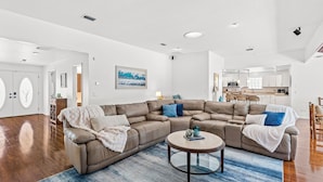 Ein großzügiges Wohnzimmer mit einer großen, bogenförmigen Couch, einem runden Couchtisch und einer Küche im Hintergrund.