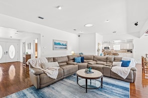 Ein großzügiges Wohnzimmer mit einer großen, bogenförmigen Couch, einem runden Couchtisch und einer Küche im Hintergrund.