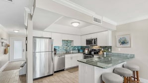 A modern kitchen with white cabinets, stainless steel appliances, a tiled backsplash, and a central island with stools. - 1045 Wave Crest Avenue (Indialantic)