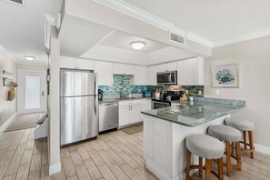 Una cocina moderna con armarios blancos, electrodomésticos de acero inoxidable, salpicadero de azulejos y una isla central con taburetes.