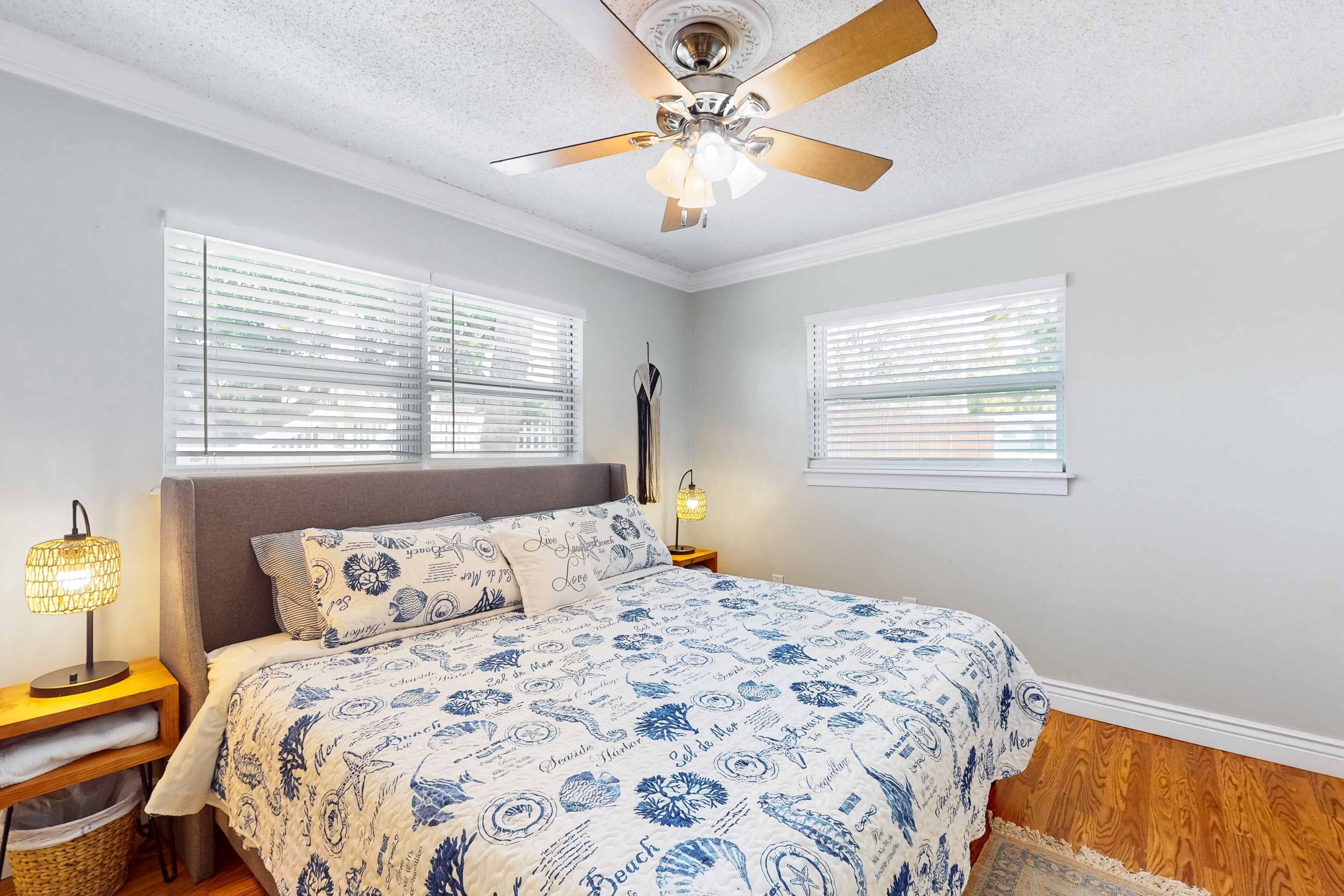A bedroom with a bed, two bedside tables, a ceiling fan, and two windows with blinds.