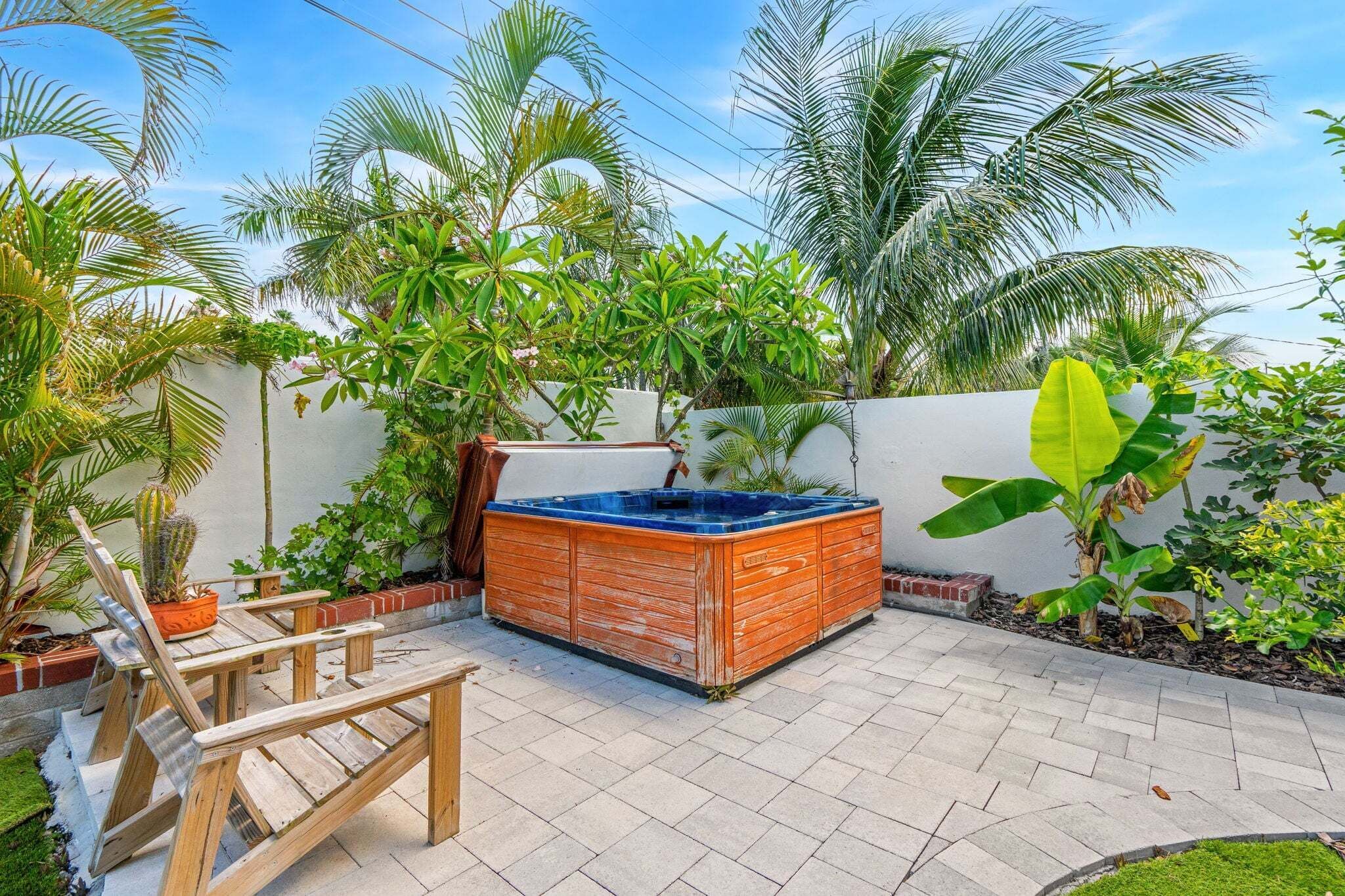 A patio with a hot tub, wooden chairs, and various tropical plants.