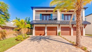 Une maison moderne à deux étages, avec une allée en briques, un patio couvert et une clôture en bois.
