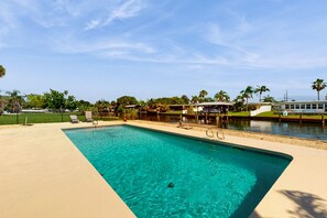 Ein rechteckiger Pool mit klarem, blauem Wasser, umgeben von einer beige farbenen Liegefläche. Liegestühle und eine kleine Brücke sind über den Pool gebaut.