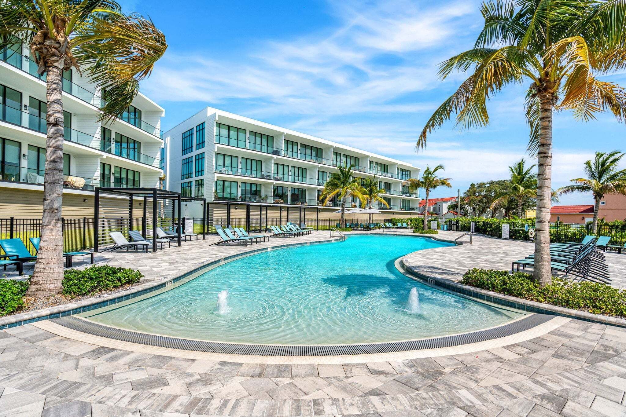 Un hôtel moderne doté d’une piscine, de palmiers et surplombant un ciel d’un bleu limpide.