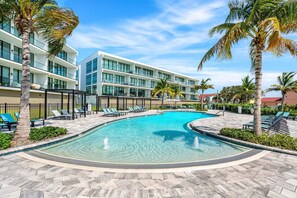 Ein modernes Hotel mit Schwimmbad, Palmen und blauem Himmel.