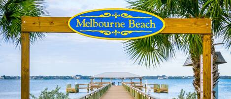 A wooden boardwalk leading to a beach area with a sign reading "Melbourne Beach."