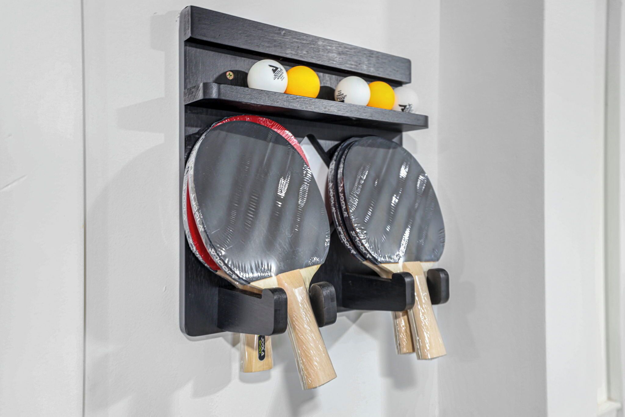 Ett väggmonterat ställ som rymmer två bordtennisracketar och ett set bordtennisbollar.