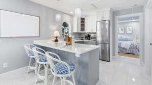 A modern kitchen with a central island, white bar stools, and pendant lighting. - 1015 Treasure Lane (Vero Beach)