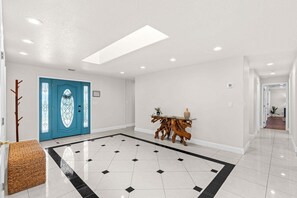A spacious hallway with a blue door, a wooden console table, and a patterned floor. - 1480 W Riviera Dr (Merritt Island)