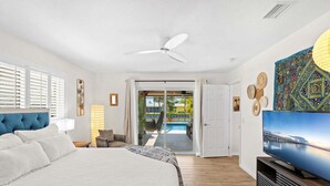 Camera d'albergo con un letto, una televisione, una ventola a soffitto e vista su piscina e area esterna.