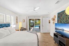 Ein Hotelzimmer mit Bett, Fernseher, Deckenventilator und Blick auf Pool und Außenbereich.