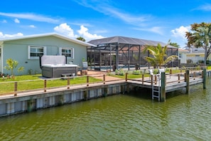 Ein Haus mit überdachter Terrasse, einem Steg über dem Wasser und einem Rasen.