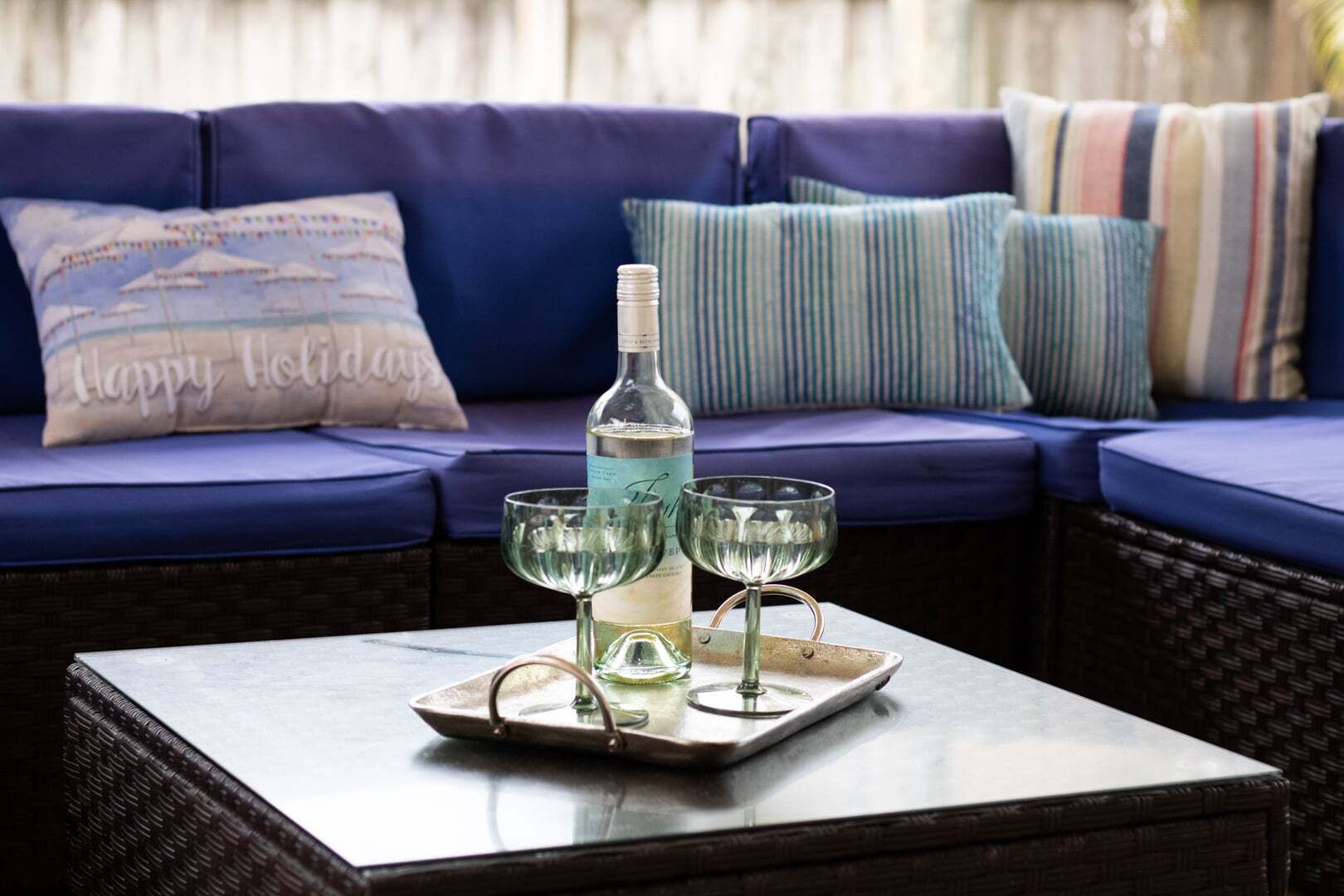 A bottle of white wine on a tray with two glasses on a table in front of a blue sofa with striped pillows.