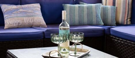 A bottle of white wine on a tray with two glasses on a table in front of a blue sofa with striped pillows.