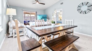A dining area with a wooden table and benches, a ceiling fan, and a view of the kitchen.