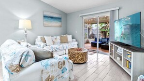 A living room with a sofa set, a television, and a view of the outdoors.