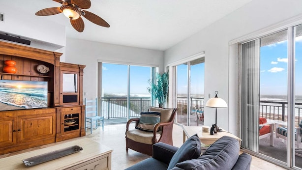 A spacious living area with a balcony, wooden furniture, and a television. - 3800 Ocean Beach Blvd, Unit 501 (Cocoa Beach)