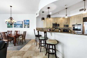A modern kitchen with a microwave, oven, and stainless steel appliances. There is a dining area with a wooden table and chairs. - 3800 Ocean Beach Blvd, Unit 501 (Cocoa Beach)