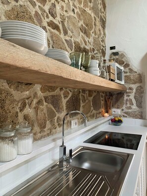 Eine Küche mit Steinwand, einem Holzbodenregal mit Tellern und Gläsern, einer Edelstahlspüle und einem eingebauten Backofen.