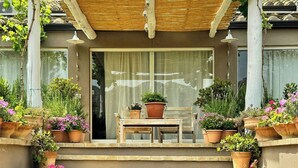 Unos escalones de piedra conducen a una pérgola de madera con una mesa y sillas debajo, rodeada de plantas en macetas.