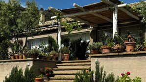 Una casa de fachada de piedra, una pérgola de madera y una variedad de plantas en macetas.
