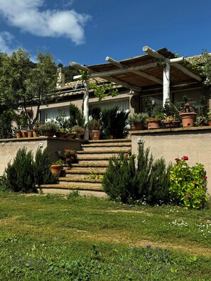 Ein Haus mit einer Steinfassade, einer Holzpergola und verschiedenen Kübelpflanzen.