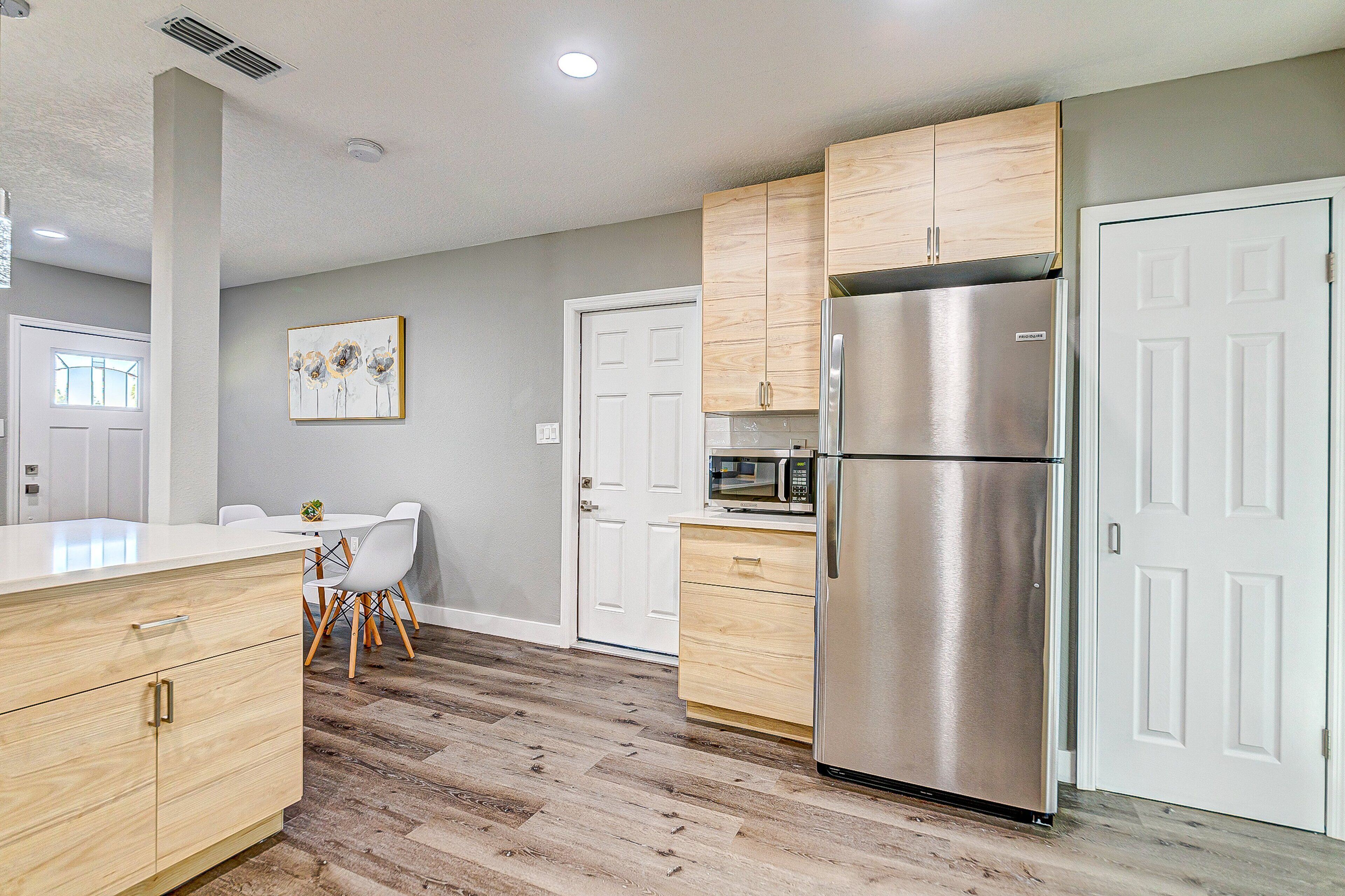 A modern kitchen with wooden cabinets, a stainless steel refrigerator, and a white countertop.