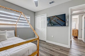 Une chambre à coucher avec un lit à baldaquin en bois, une grande fenêtre avec des stores, une porte et une œuvre d’art accrochée au mur.