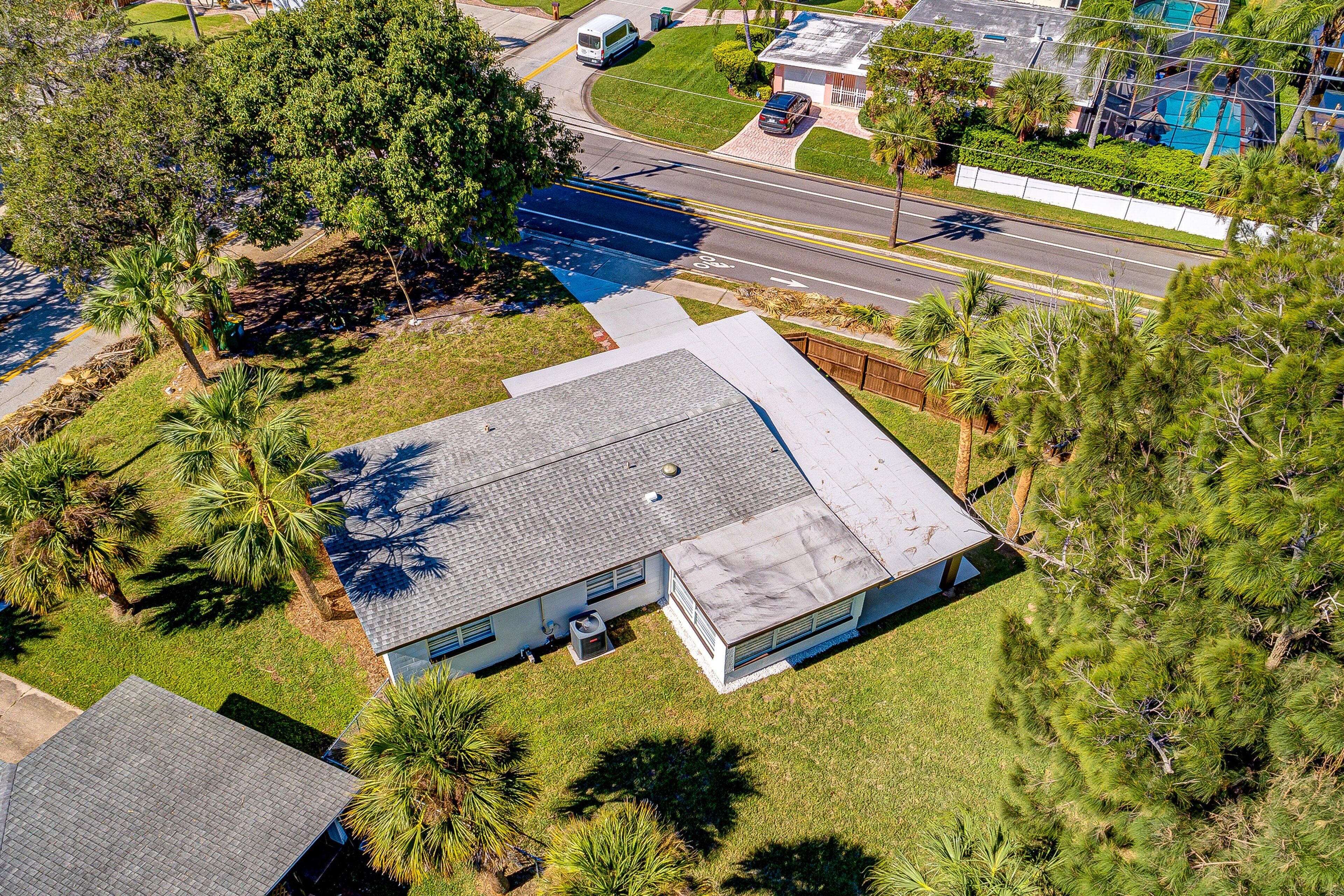 An aerial view of a residential property with a sloped roof, surrounded by palm trees and a well-maintained lawn.