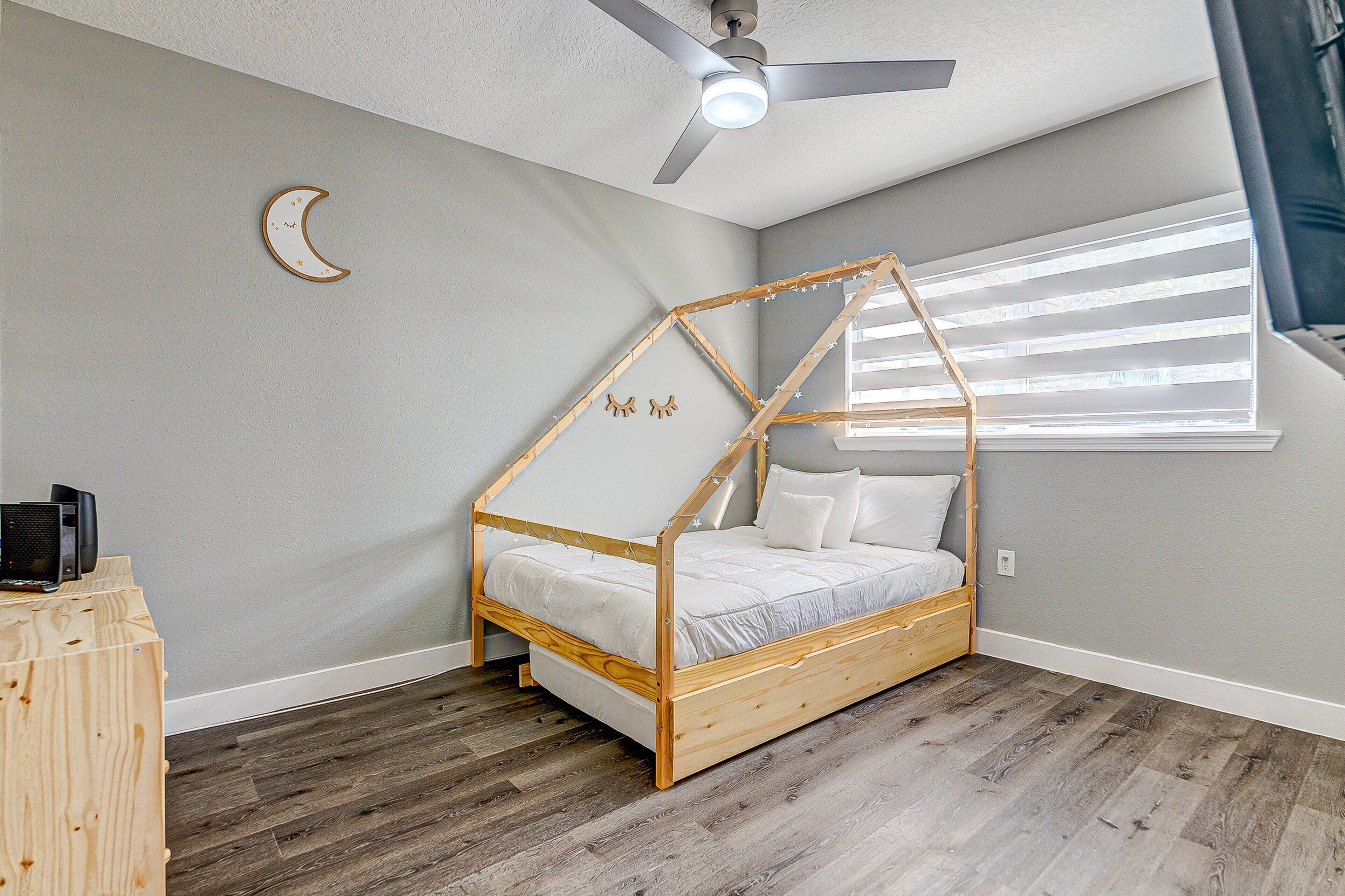 Un dormitorio con estructura de cama de madera, ventilador de techo, luz nocturna y ventana con persianas.