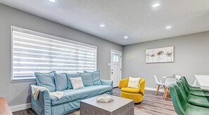 Un salon moderne avec un canapé, un fauteuil jaune, des chaises vertes, une table basse et un tableau accroché au mur.