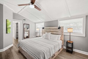 Een slaapkamer met een bed, een plafondventilator, een nachtkastje, een lamp, een raam met zonwering, en een deur naar een inloopkast.