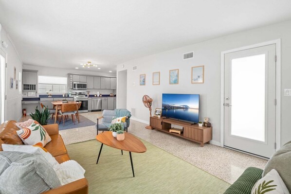 A modern living room with a sofa, coffee table, TV, and a dining area with chairs and a table.