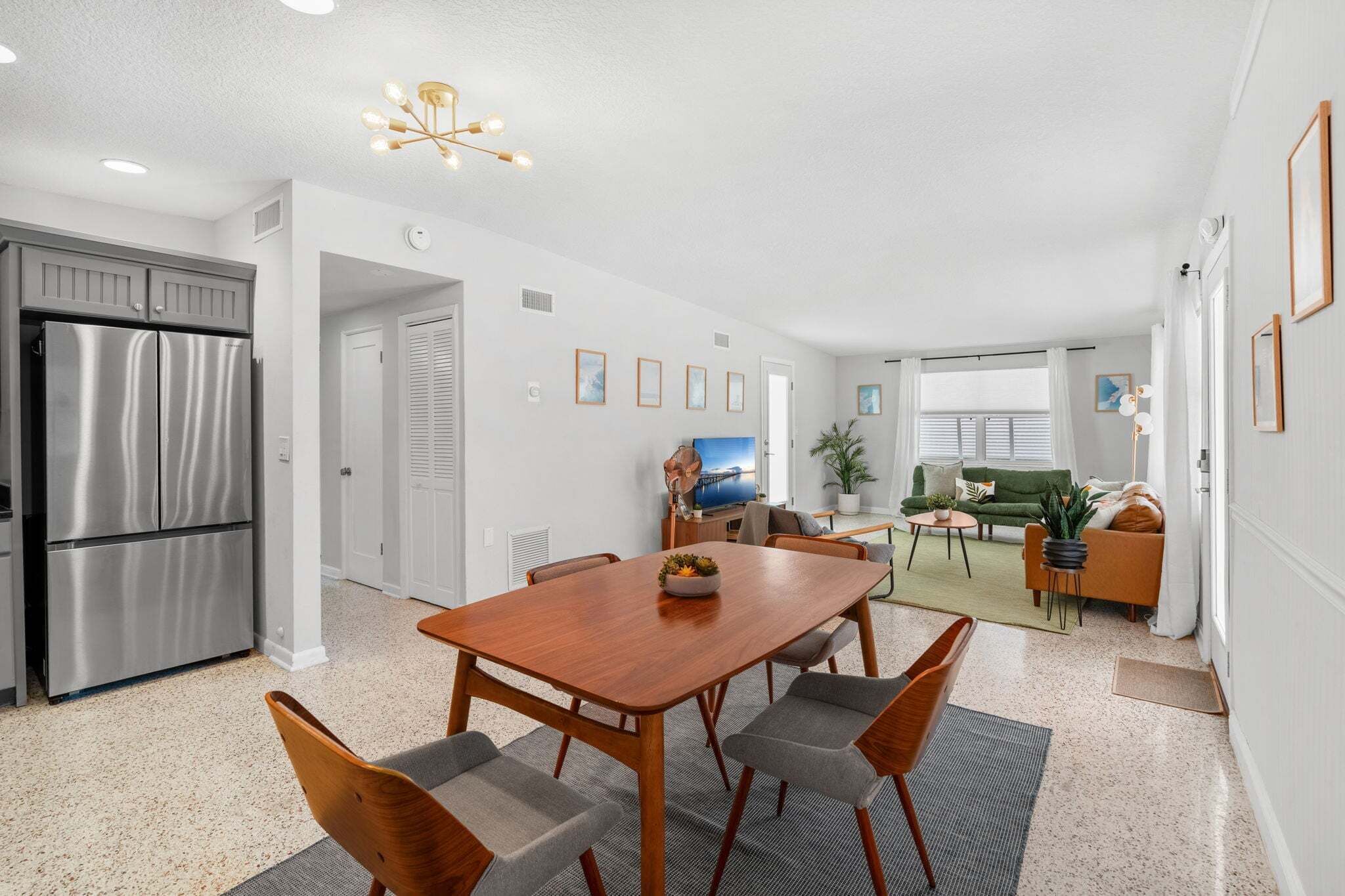 Eine moderne Küche mit einem Edelstahl-Kühlschrank, einem Holzesstisch mit vier Stühlen und einem Wohnbereich mit Sofa und Couchtisch.
