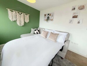 A bedroom with a bed, a grey sofa, a macrame wall hanging, and a wall with framed pictures. - Penthouse with City Views (Bristol City)