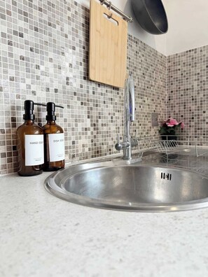 A kitchen with a stainless steel sink, two soap bottles, a hanging pot rack, and a tiled backsplash. - Penthouse with City Views (Bristol City)