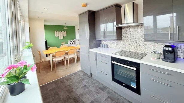 Een moderne keuken met grijze kastjes, een zwarte oven en een koffieapparaat.