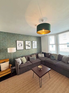 Ein Wohnzimmer mit Ecksofa, einem kleinen Tisch und Wandbildern.