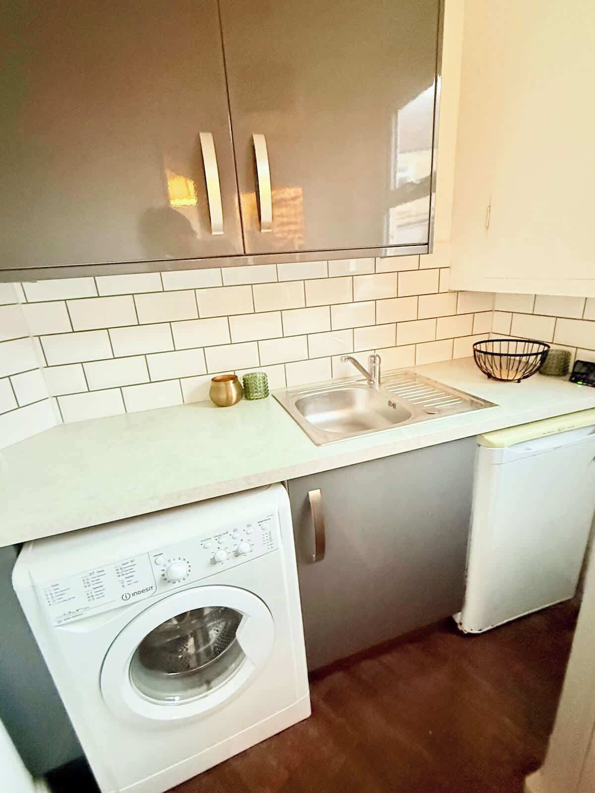 A compact kitchen with a washing machine, a sink, and cabinets.