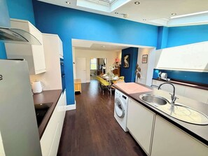 Une cuisine moderne équipée d’un lave-linge, d’un évier et d’un coin repas avec des chaises jaunes.