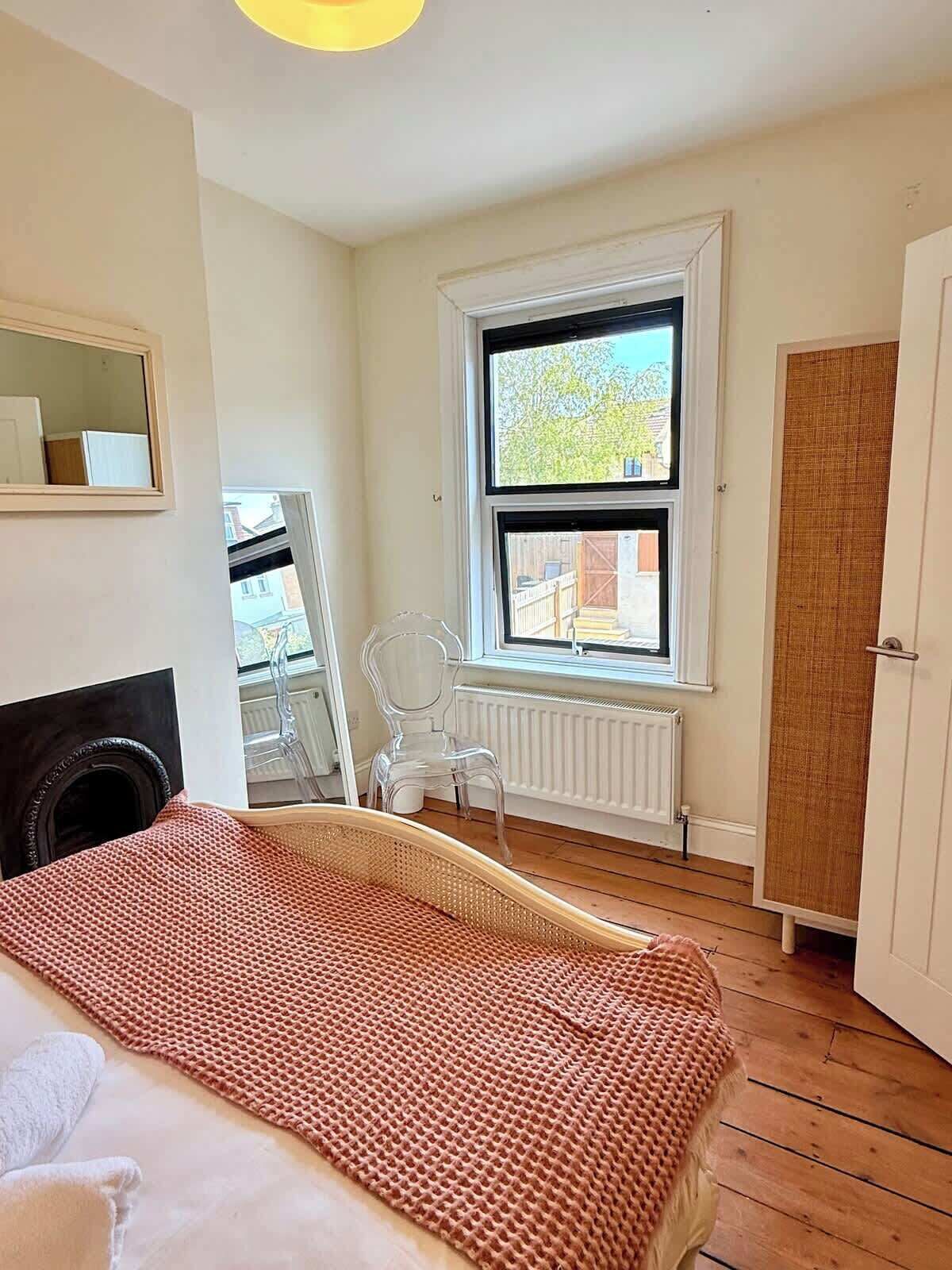 A bedroom with a bed, a window, a radiator, a chair, and a door.