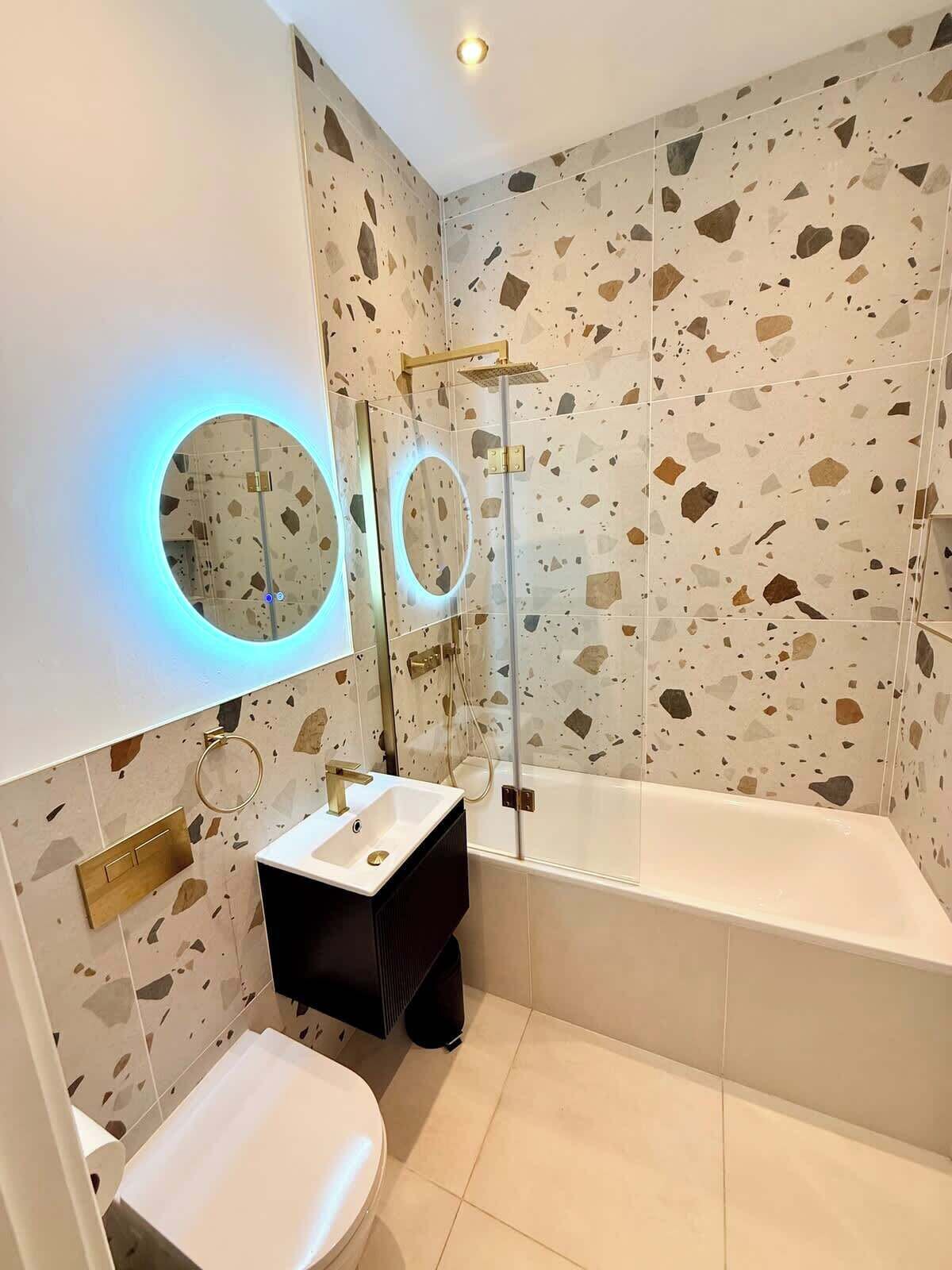 Ein Badezimmer mit freistehender Badewanne, einem runden Spiegel mit Beleuchtung und einer Toilette.